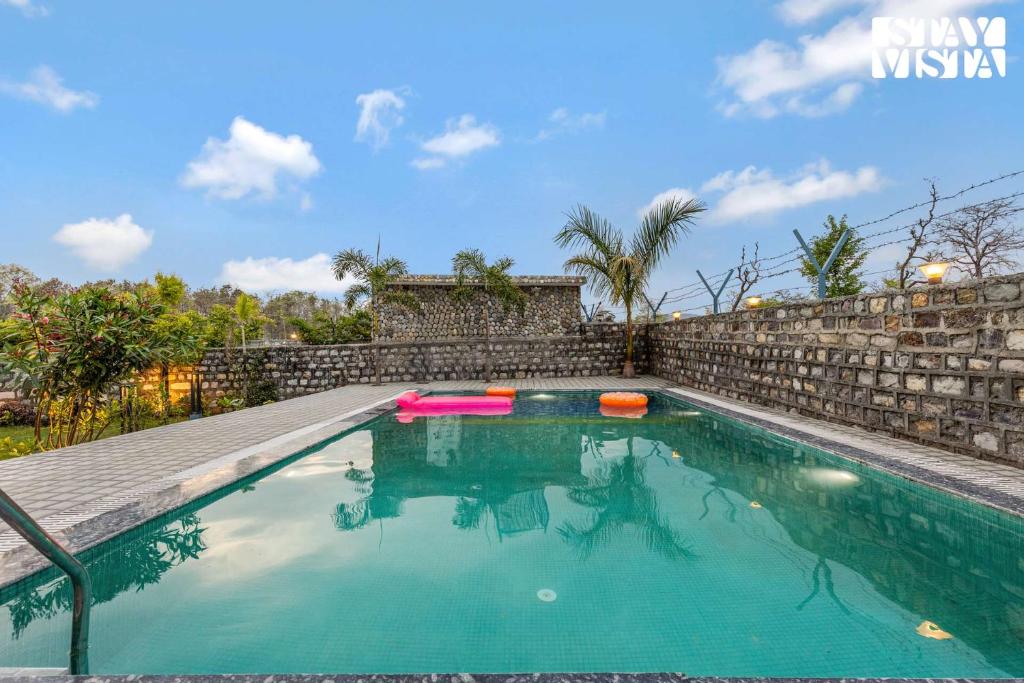 a swimming pool in a backyard with a stone wall at Corbett Calling with Jacuzzi & Projector Set-Up by StayVista in Rāmnagar
