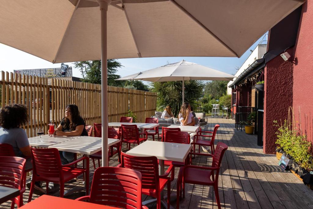 personnes assises à des tables avec des parasols sur un patio dans l'établissement ibis Bordeaux Mérignac, à Mérignac