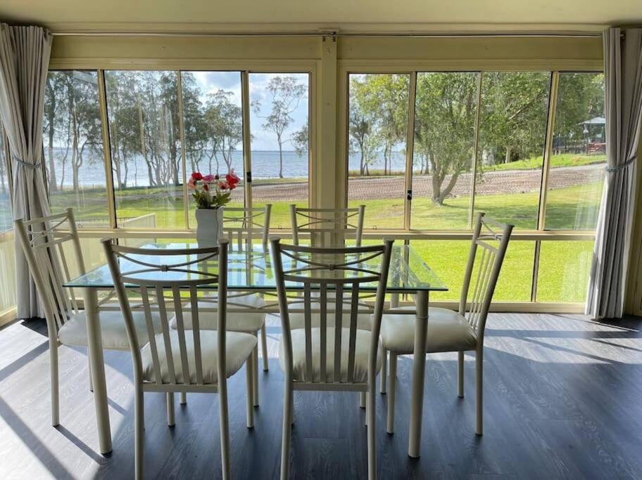 comedor con mesa de cristal y sillas en Aircabin - Tuggerawong - Lake Front - 3 Beds House, en Rocky Point