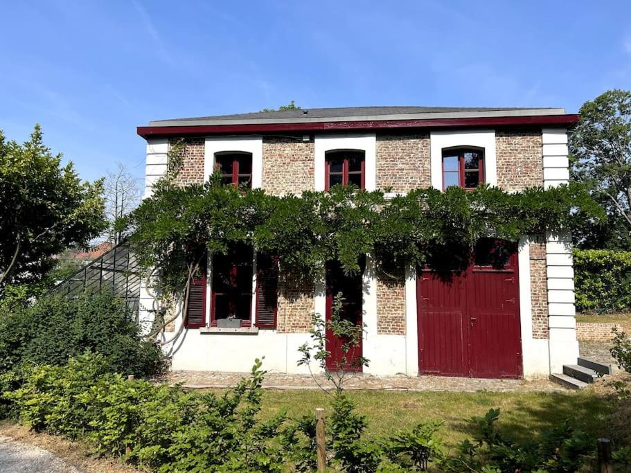 uma antiga casa de tijolos com portas vermelhas e videiras em Charmante maison dans un coin de verdure à Boitsfort em Bruxelas