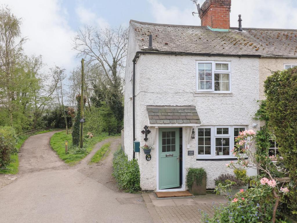 a white house with a green door and a dirt road at Periwinkle Cottage in Loughborough