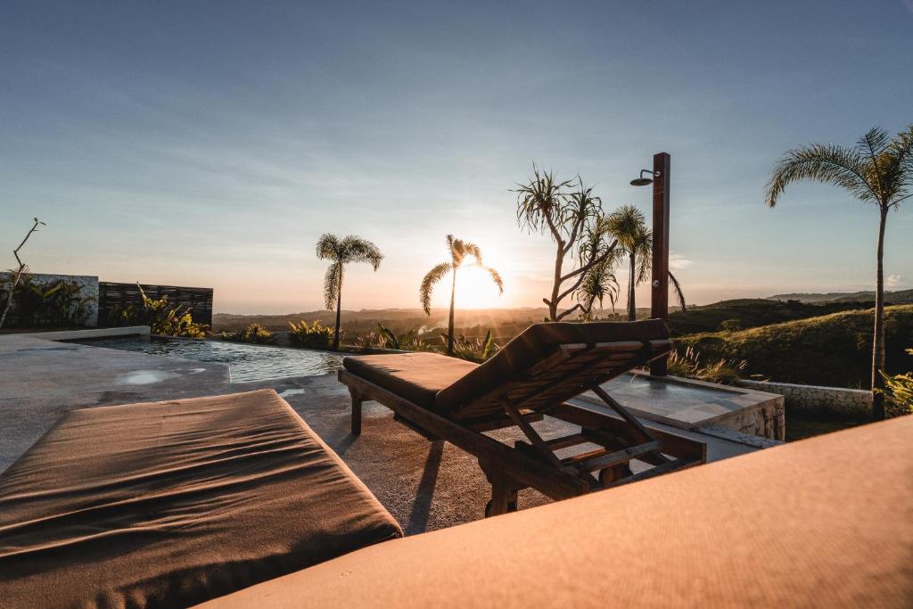 a patio with a table and a bench and palm trees at Sundance Residence Nusa Penida - 2 Bedroom with Private Pool Villa in Tanglad