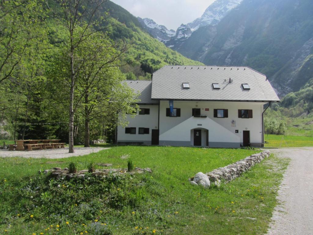 a white house in a field with mountains in the background at PUS Bavšica in Log pod Mangartom