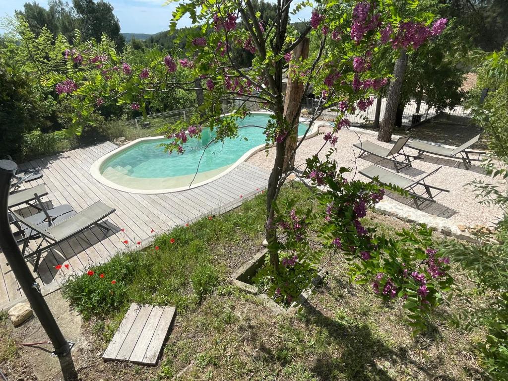 une piscine avec des bancs et un arbre avec des fleurs violettes dans l'établissement Mas du Puech Cymbale, à Assas
