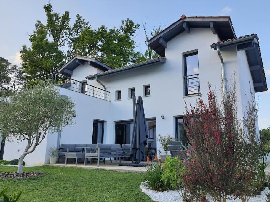 Cette maison blanche dispose d'une terrasse et d'un parasol. dans l'établissement MAISON CONTEMPORAINE à 5KM DE BIARRITZ AVEC JACUZZI, à Bassussarry