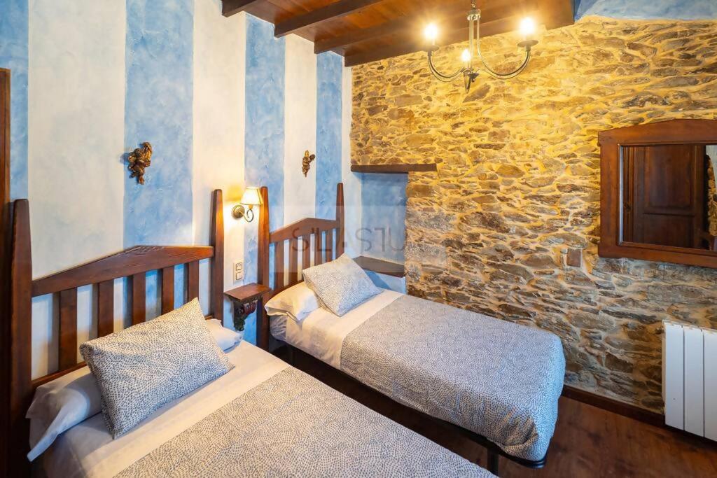 1 dormitorio con 2 camas y pared de piedra en La Casona Del Cura II, en Pravia