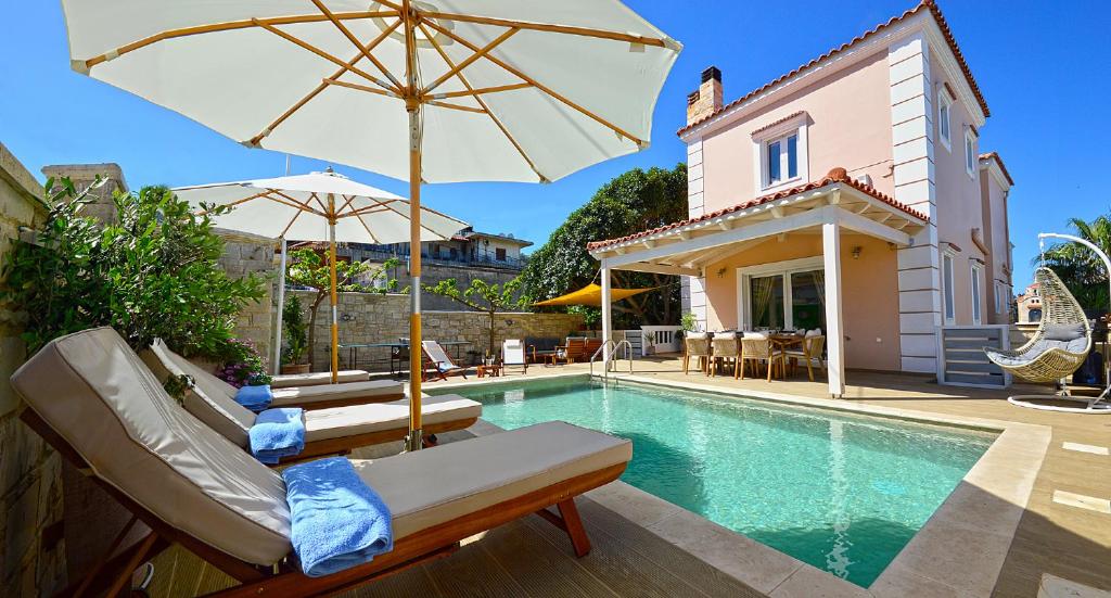 a pool with chairs and an umbrella next to a house at Villa Ithaca in Varípetron