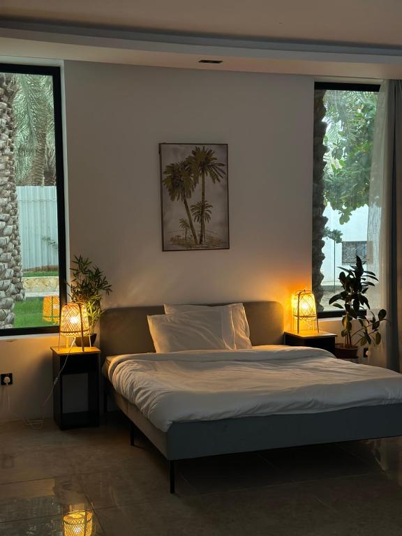 a bedroom with a bed with two lamps and two windows at منتجع ريتام in Al Ahsa