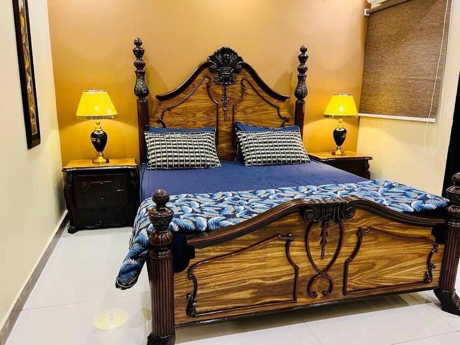 a bedroom with a large wooden bed with two lamps at Bahria Town Lahore - NEXT INN Two Bedroom condo with free parking 203 in Lahore