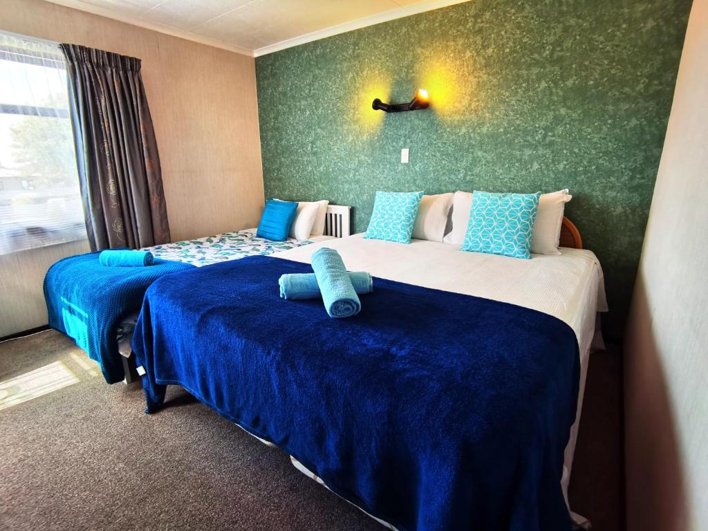a hotel room with two beds with blue sheets at Denby Golf House Tikipunga in Whangarei
