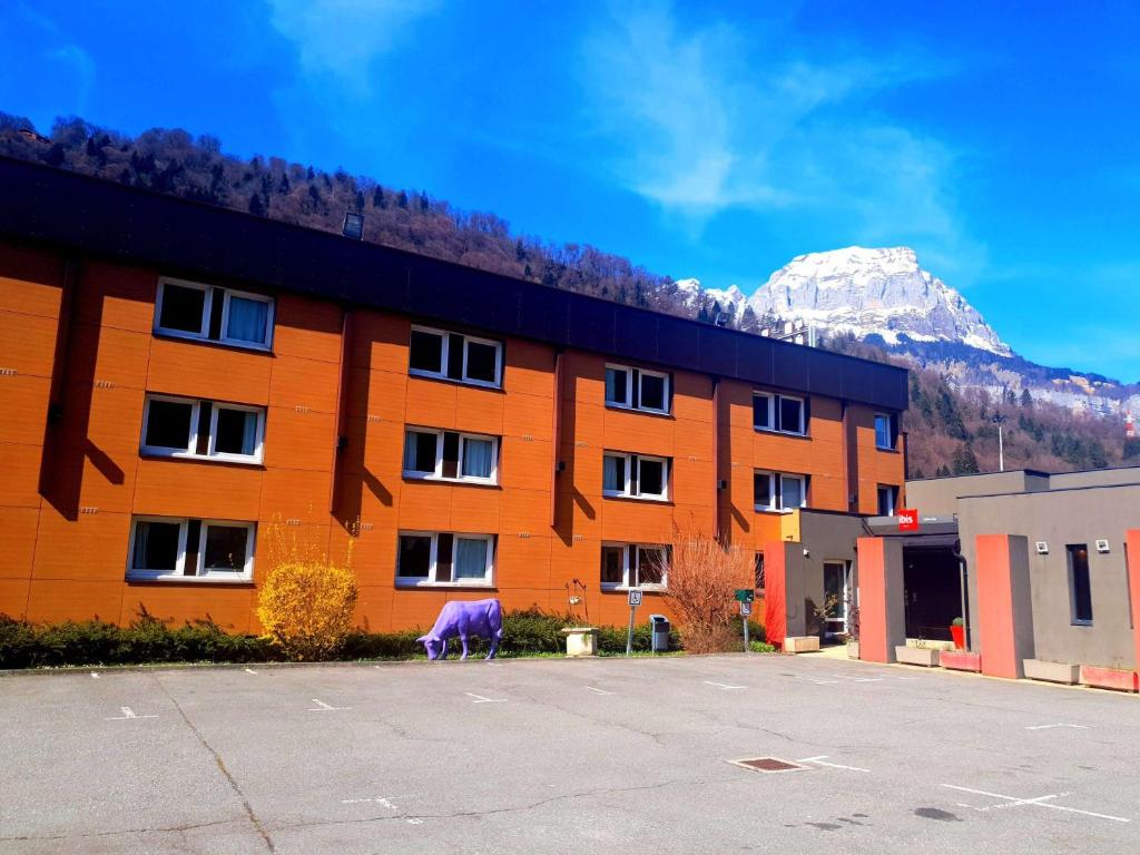 a large orange building with a mountain in the background at Ibis Hôtel Sallanches in Sallanches
