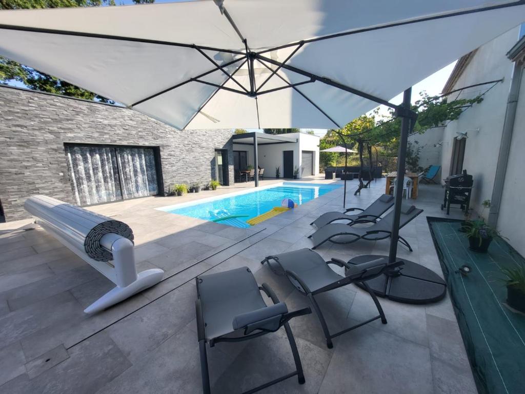 eine Terrasse mit Stühlen, einem Sonnenschirm und einem Pool in der Unterkunft Le Mas De Poujoles in Caussade