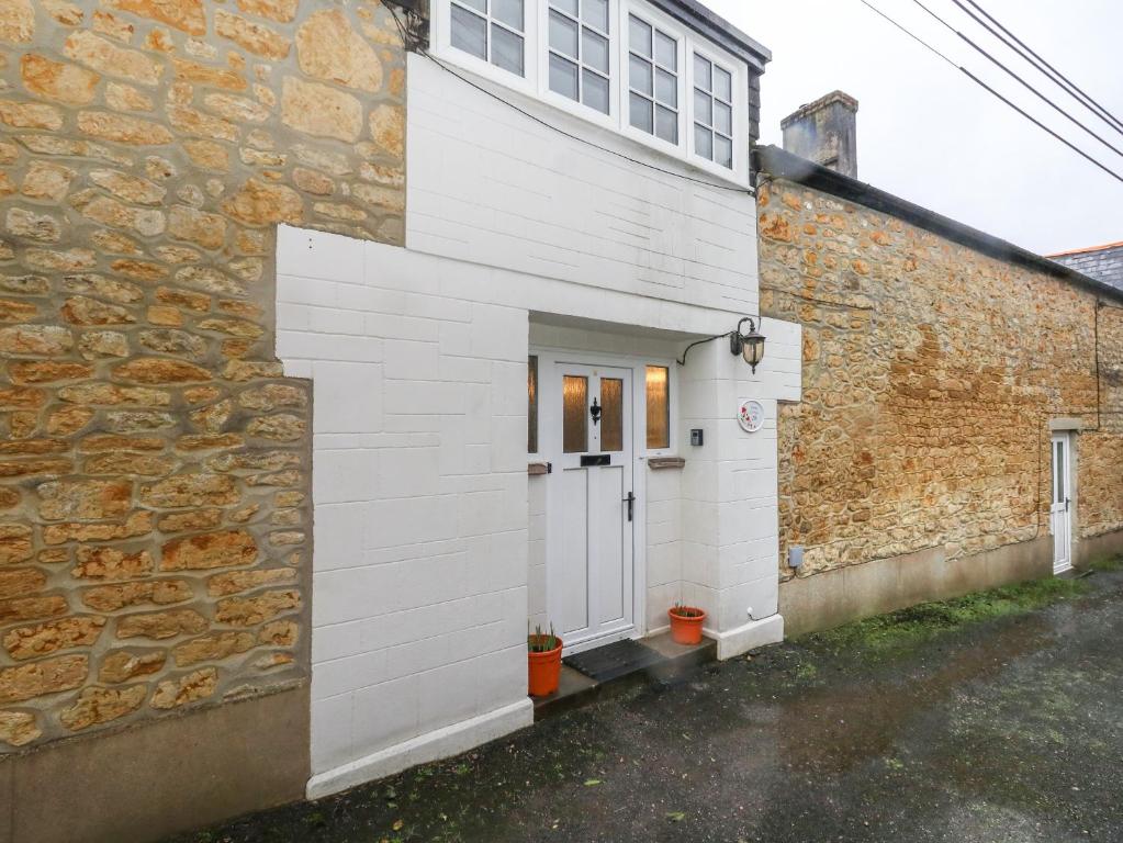 a white house with a door and a stone wall at Poppy Cottage in Beaminster