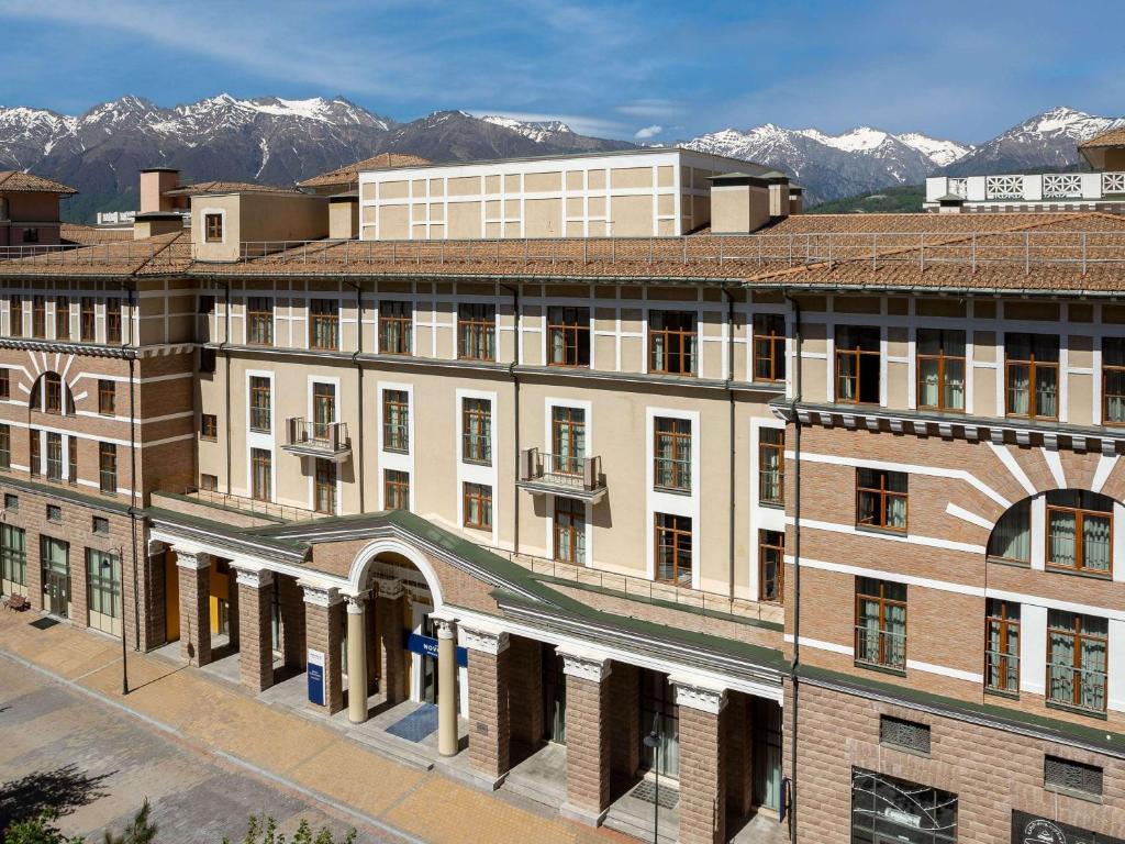 a large building with snow covered mountains in the background at Novotel Congress Krasnaya Polyana in Estosadok