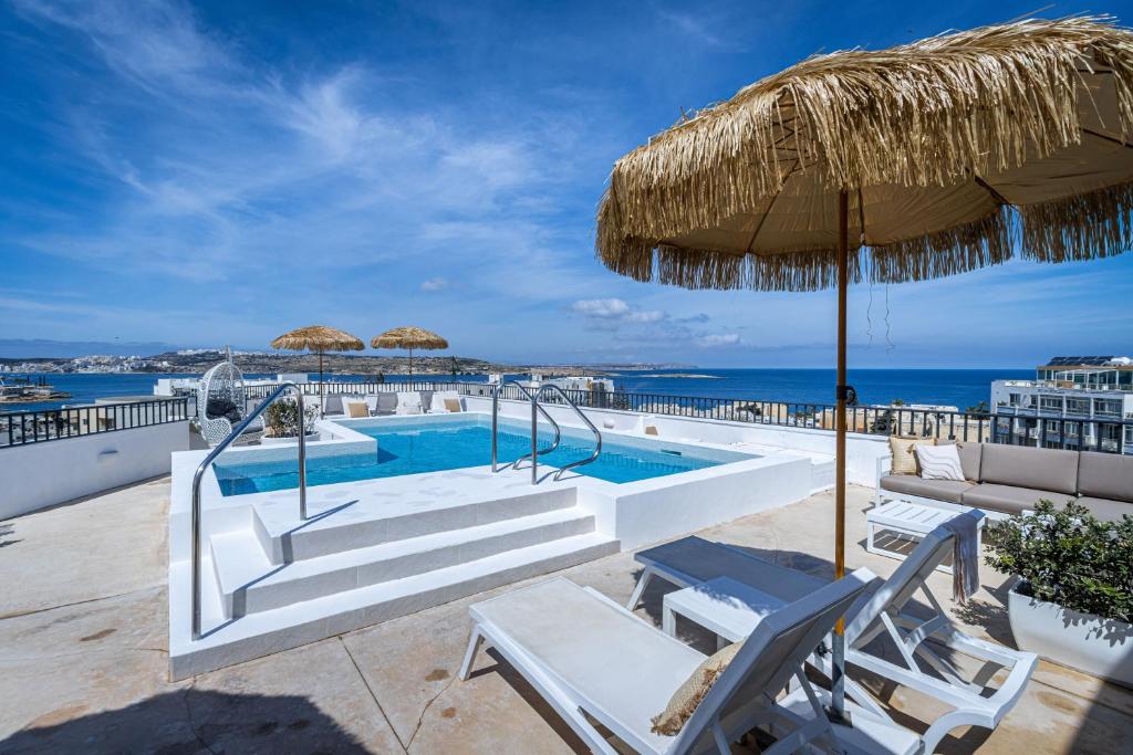 - une piscine avec un parasol et des chaises en paille dans l'établissement Park Lane Boutique Aparthotel, à San Pawl il-Baħar