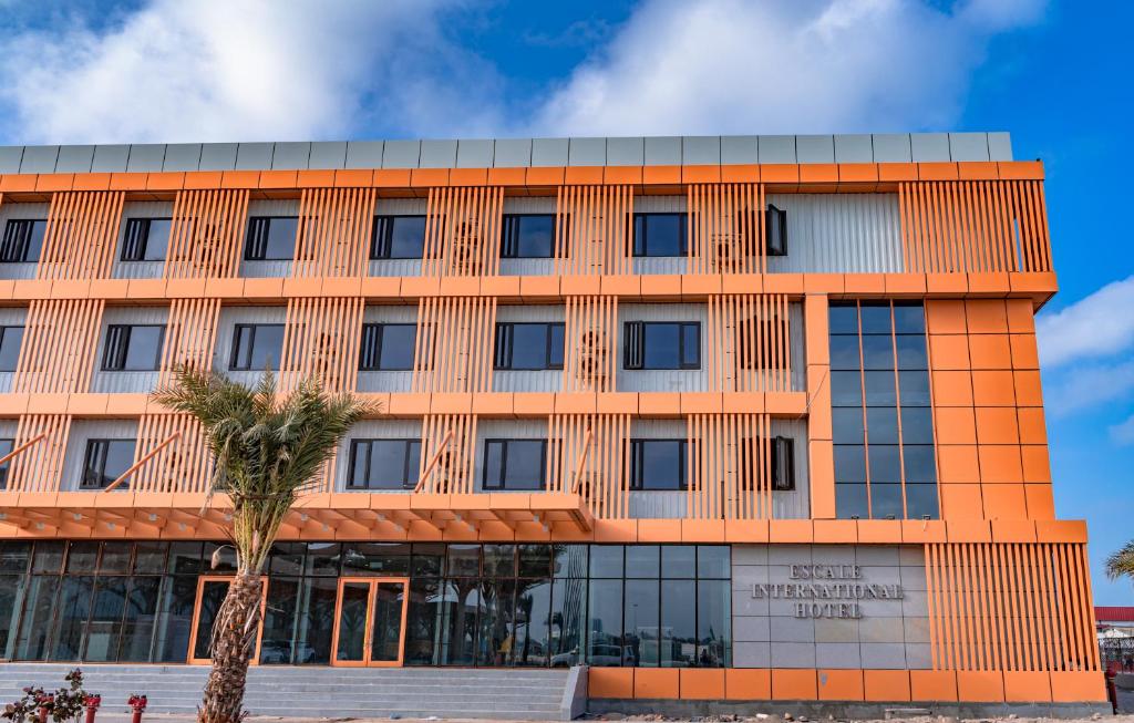 an orange building with a palm tree in front of it at Escale International Hotel in Djibouti