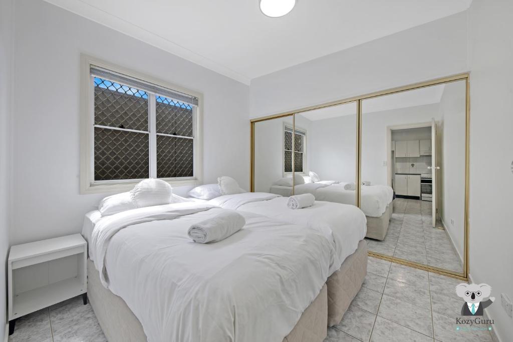 a white bedroom with two beds and a large mirror at Fairfield 1B Granny Flat Sleep up to 4 ppl in Fairfield