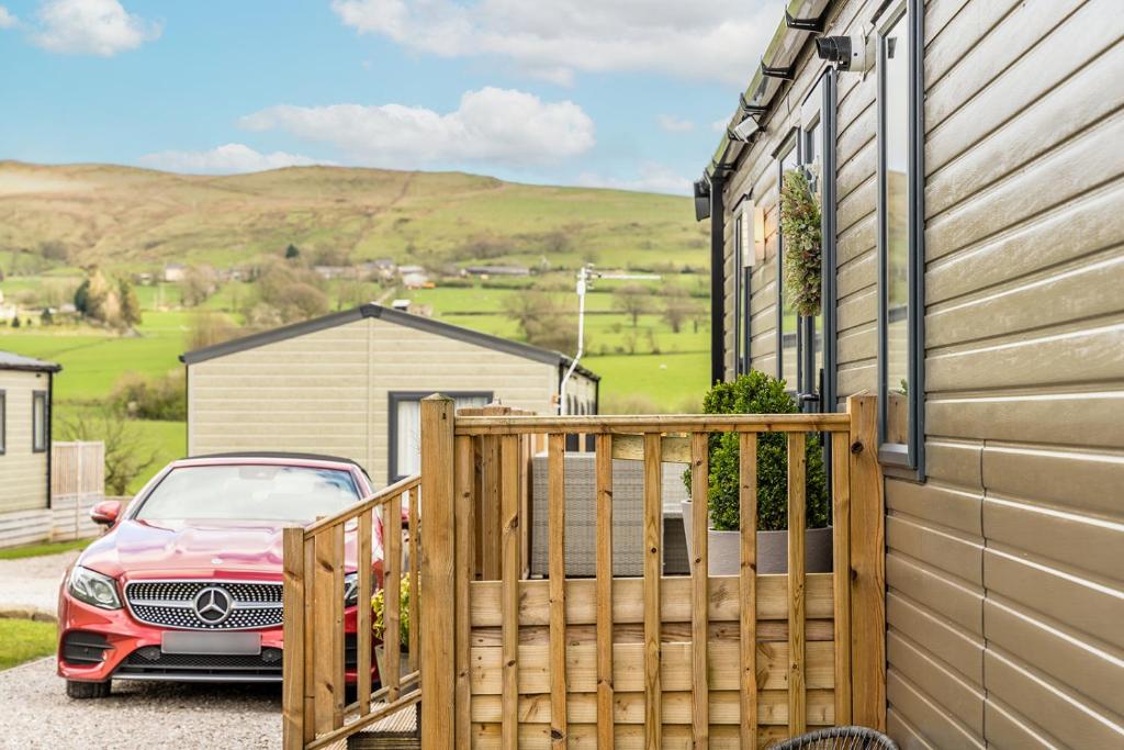a red car parked next to a house with a fence at Wiswell View Lodge: Pendle View Holiday Park in Clitheroe