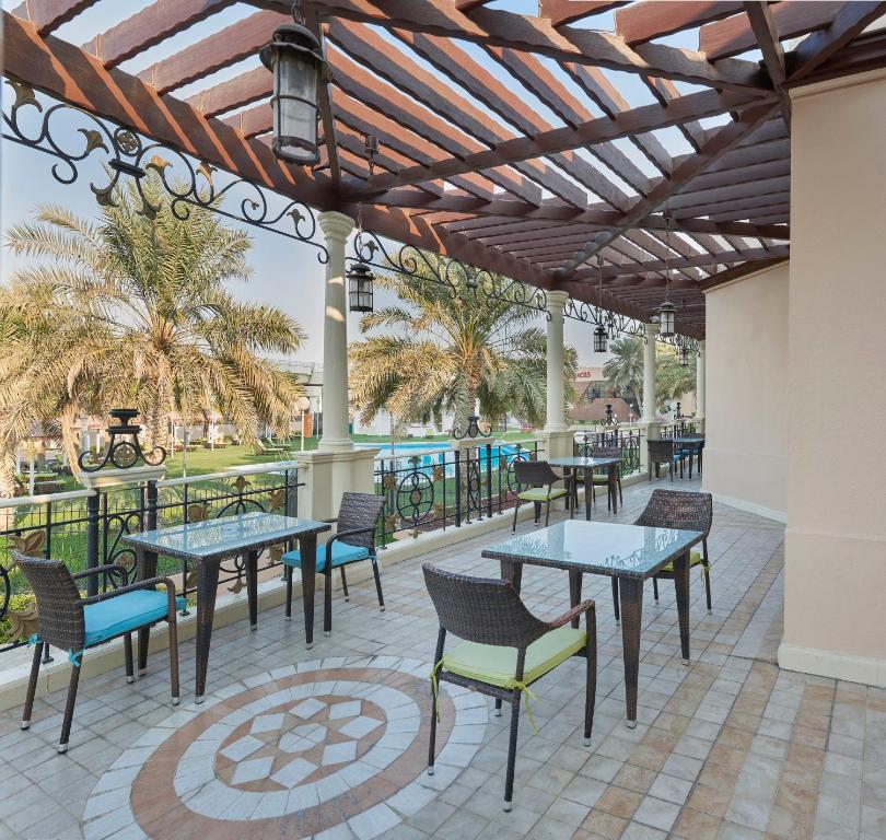 a patio with tables and chairs and palm trees at Crowne Plaza Bahrain by IHG in Manama