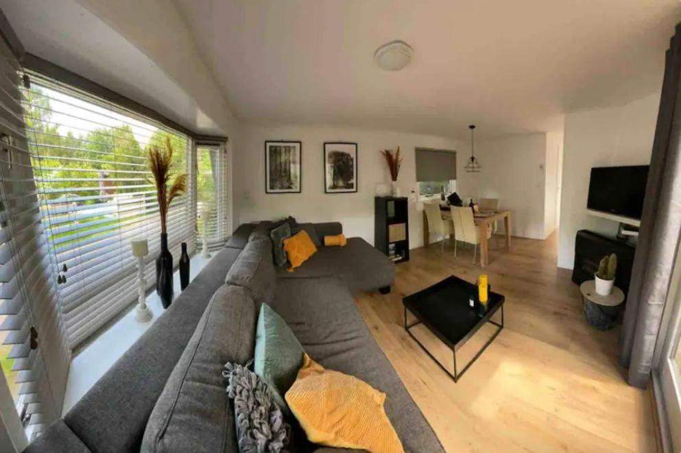 ein Wohnzimmer mit einem grauen Sofa und einem Tisch in der Unterkunft Heerlijk chalet midden in de natuur in Putten