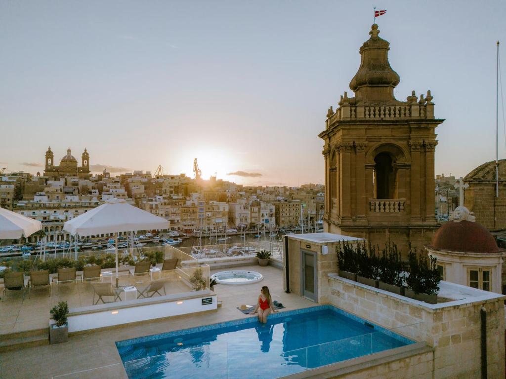 una donna in piedi accanto a una piscina in un edificio di IBB Hotel Palazzo Bettina Malta a Birgu (Vittoriosa)