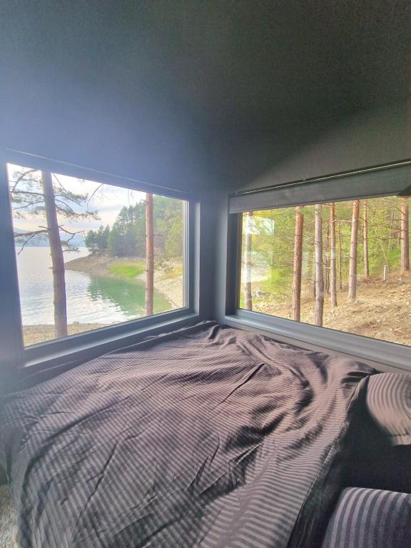 a bedroom with a bed and two large windows at Nomad Lake Cabins in Rugineşti