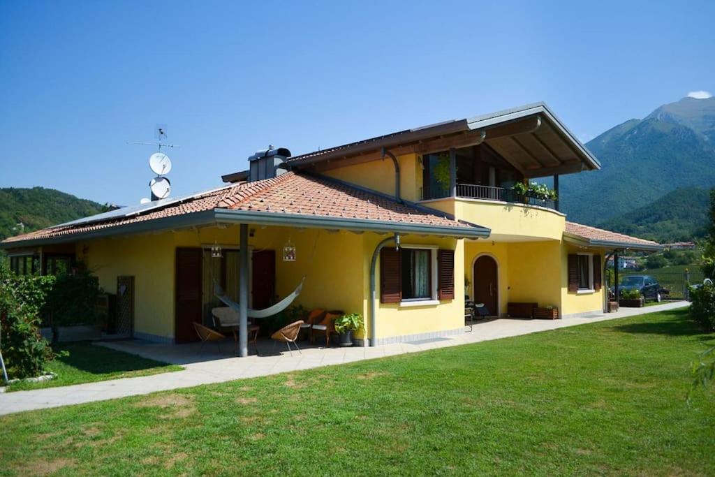 una casa amarilla con un césped verde delante de ella en Villa Eugenia, dove la pace è di casa, en Drena