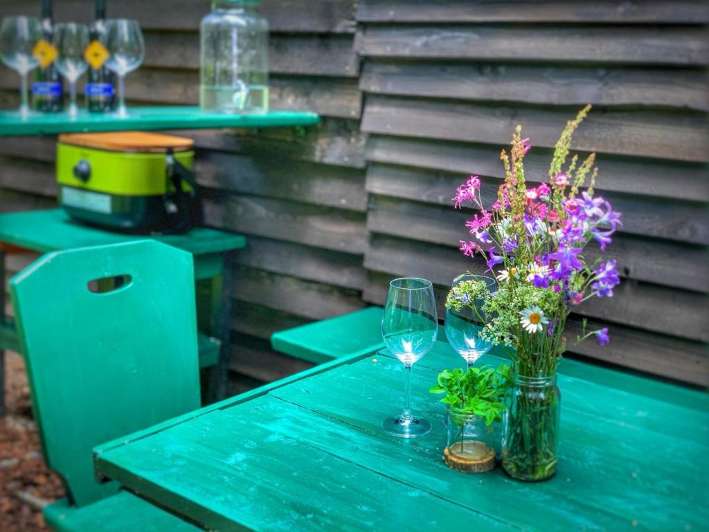 a blue table with a vase of flowers and wine glasses at VLES chata uprostřed lesa in Prachatice