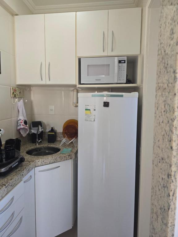 W kuchni znajduje się biała lodówka i kuchenka mikrofalowa. w obiekcie Hospedagem Flat verde Sul de Minas w mieście Caxambu