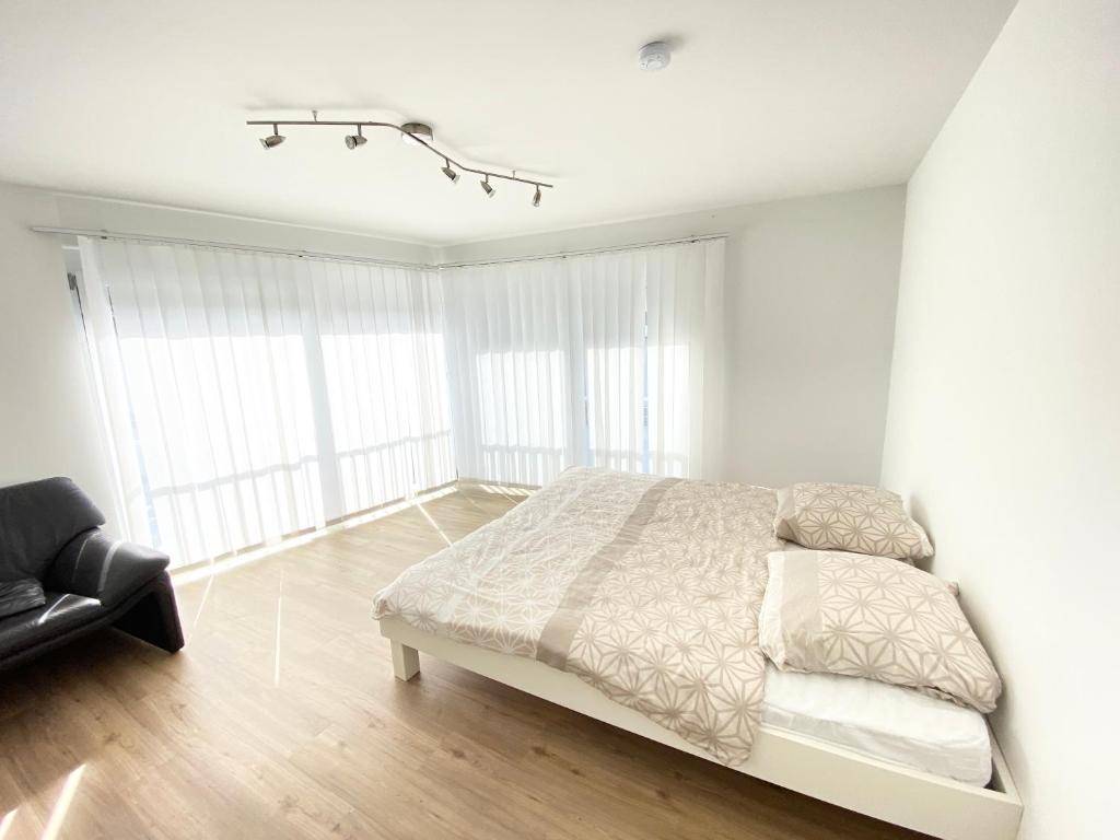 ein weißes Schlafzimmer mit einem Bett und einem Stuhl in der Unterkunft Modern One Bedroom + Bathroom Apartment, 10 min from Basel City in Grenzach-Wyhlen
