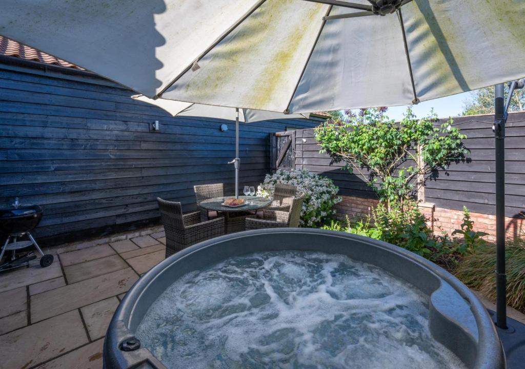 a hot tub with an umbrella on a patio at Partridge Lodge in Reepham