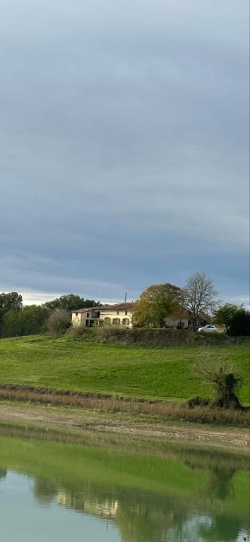 une maison dans un champ à côté d'une masse d'eau dans l'établissement DOMAINE DU LAC DE MONTPITOL, à Verfeil