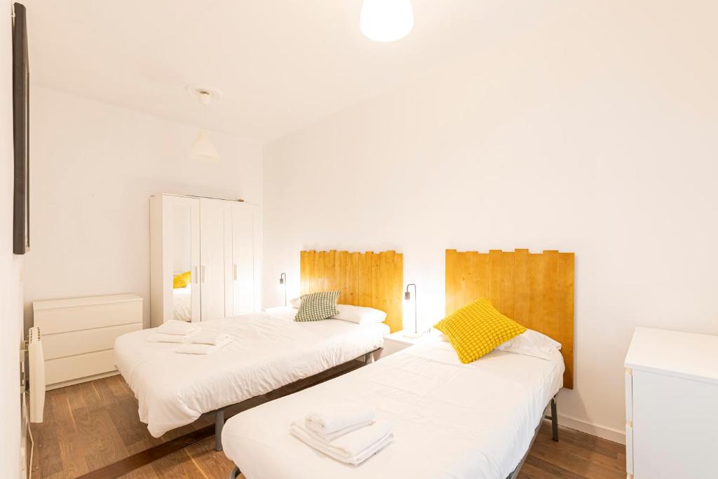 マドリードにあるApto Madrid Confort Centroの白い壁とウッドフロアの客室で、ベッド2台が備わります。