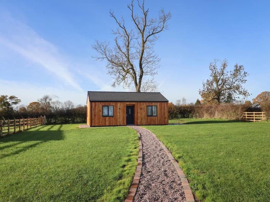 a small wooden cabin in a field with a tree at Oak Lodge in Ashbourne