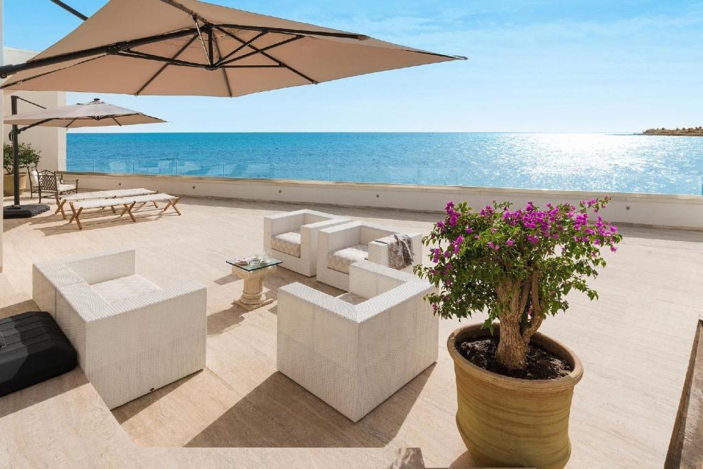 une terrasse avec des chaises blanches et un parasol et l'océan dans l'établissement Ferienhaus für 6 Personen ca 100 qm in Cicirata, Sizilien Ostküste von Sizilien, à Avola