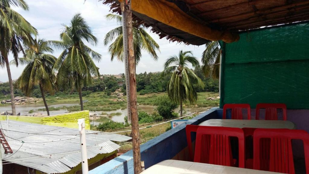 un restaurante con sillas rojas, una mesa y palmeras en Riverside Homestay, en Hampi