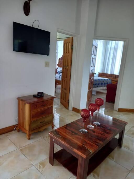 a living room with a wooden table and red wine glasses at Kassion Corner Montego bay in Montego Bay