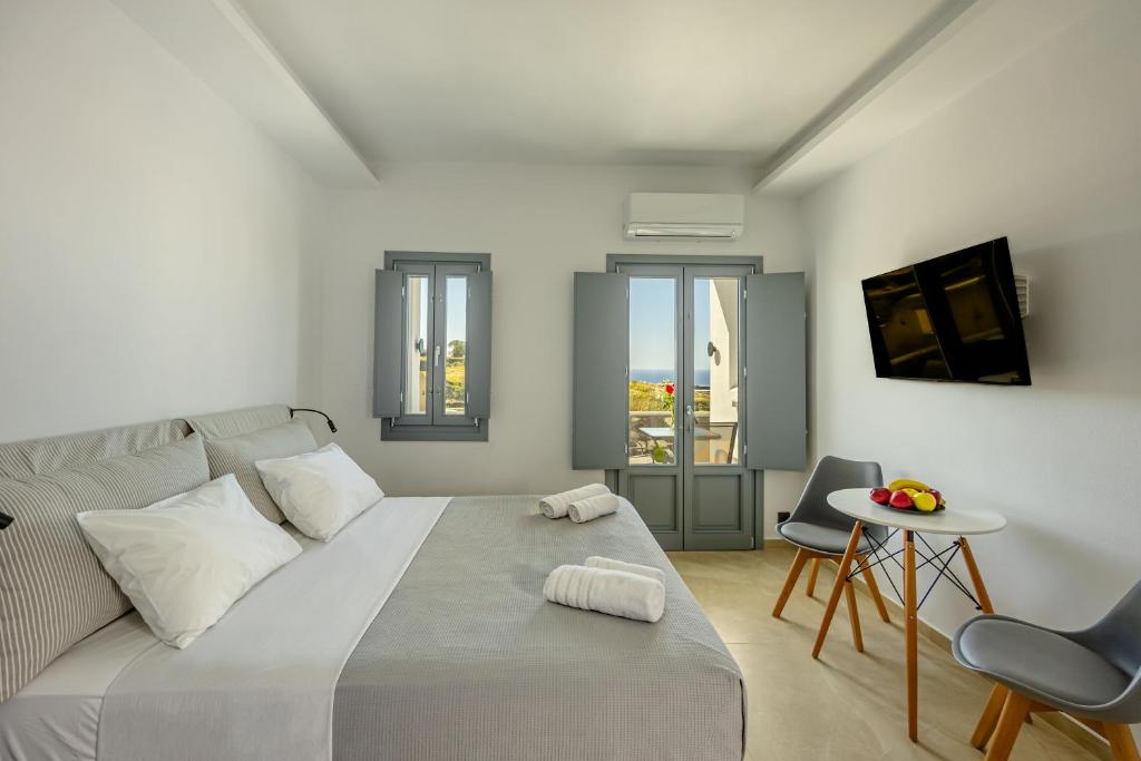 Nastram Suites Oia في أويا: غرفة نوم بيضاء بسرير وطاولة وكراسي