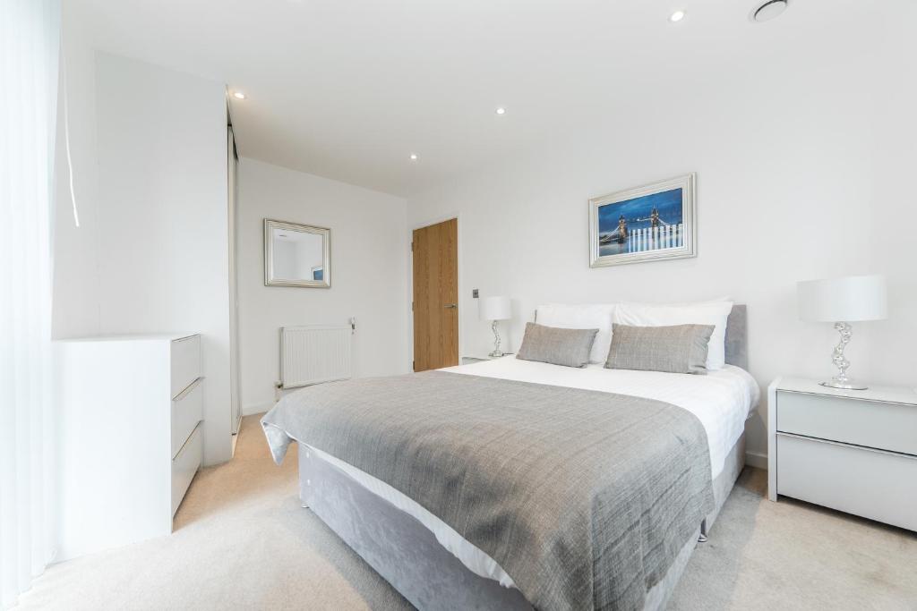 a white bedroom with a large bed and a tv at Apartments Near The O2 in London