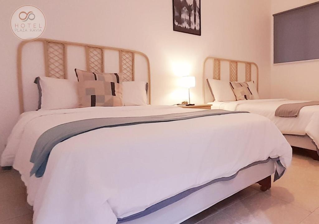 um quarto com 2 camas grandes com lençóis brancos e almofadas em Hotel Plaza Kavia em Santo Domingo