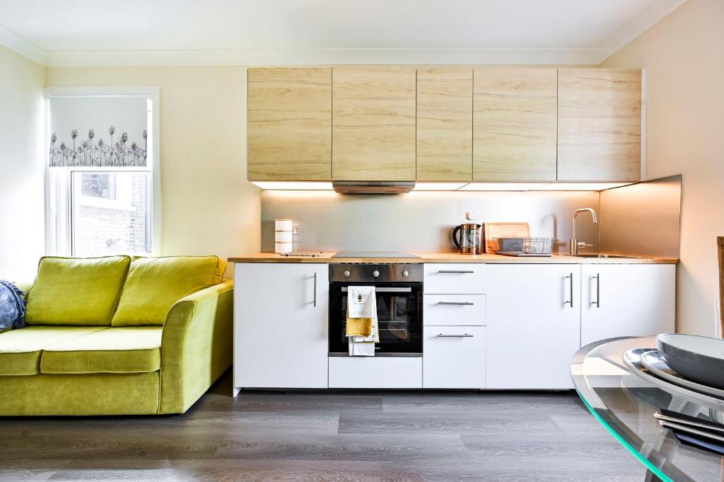 a kitchen with white cabinets and a green couch at Luxury two bedroom a stride away from Meridian Greenwich in London