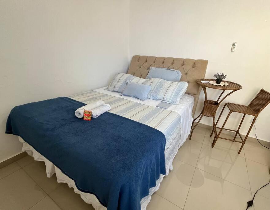 a bedroom with a bed with a blue blanket and a table at Apartamento Salvador/200m da praia. in Salvador