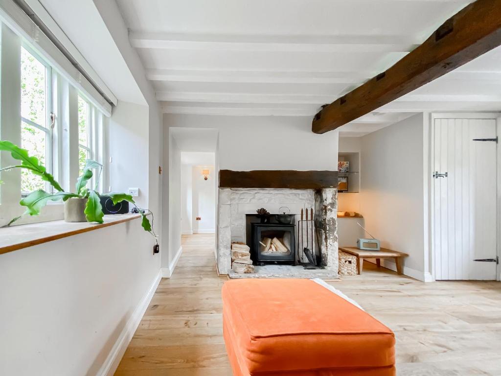 an orange ottoman in a living room with a fireplace at Oasis Cottage in Broughton Gifford