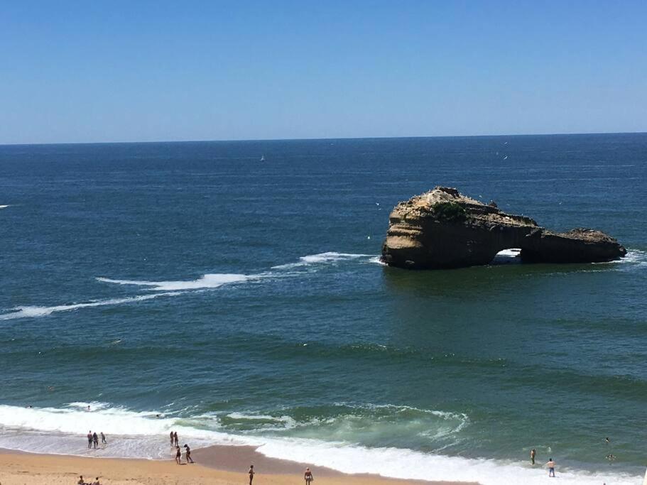 un groupe de personnes debout sur la plage près d'un rocher dans l'océan dans l'établissement superbe studio MIRAMAR plein sud, pieds dans l'eau, à Biarritz