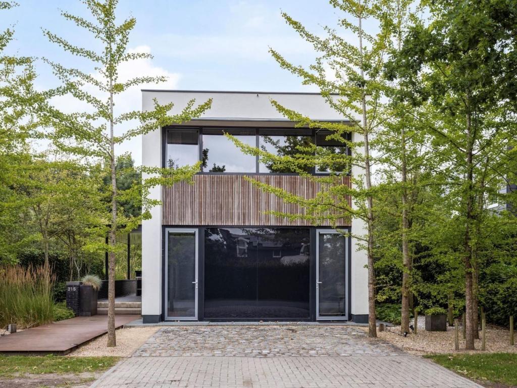 ein modernes Haus mit Glastüren und Bäumen in der Unterkunft Wellness villa on the water near Harderwijk in Zeewolde