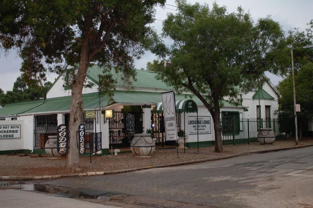 a white building with a green roof and trees at Lockerbie Lodge in Vryburg