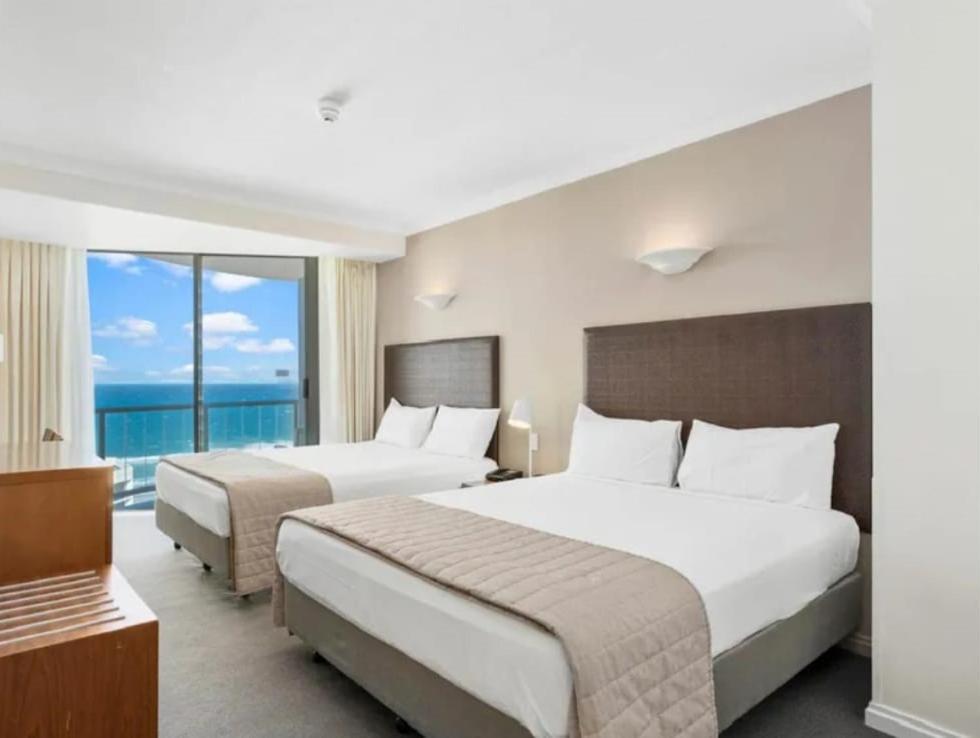 two beds in a hotel room with a view of the ocean at Serain Residences on Legends in Gold Coast
