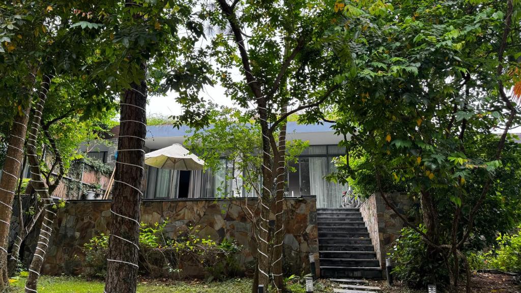 una casa con escaleras y un paraguas detrás de algunos árboles en Flamingo Đại Lải Resort - Bách Thanh C16, en Phúc Yên