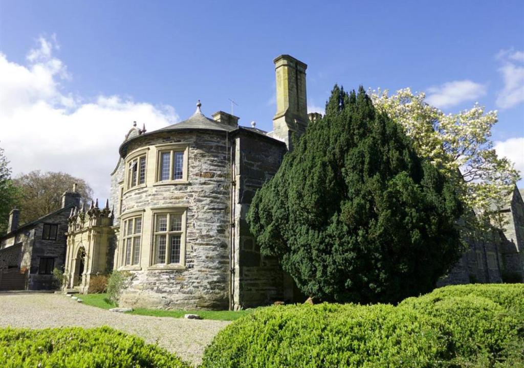 una vieja casa de piedra con un árbol delante en The Manor Criccieth, en Porthmadog