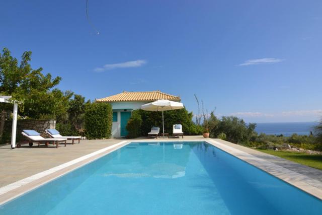 ein blauer Pool mit Sonnenschirm und ein Haus in der Unterkunft Icon Painter Villa 'Peroulia 4' in Kómboi